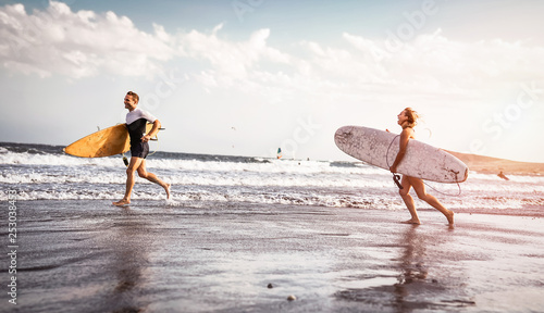 Photography Happy surfers running with surfboards along the sea shore - Sporty couple having