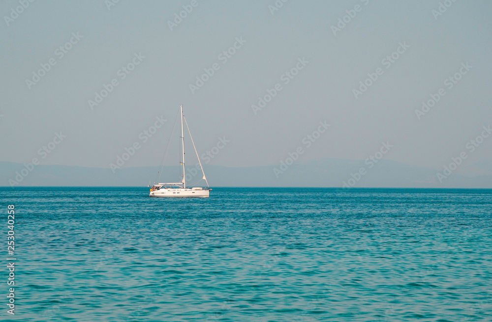 Yacht sailing on opened sea with hills on background. Sailing boat floating on sunnyday- Image. Sailing boat on sea with crystal blue water.  Beautiful scenic photo of boat on the sea.