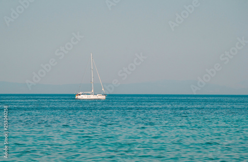 Yacht sailing on opened sea with hills on background. Sailing boat floating on sunnyday- Image. Sailing boat on sea with crystal blue water. Beautiful scenic photo of boat on the sea.