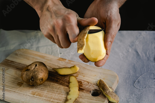 The chef cleans potatoes. For dishes with potatoes. On a black background, the concept of the menu, cooking, healthy eating