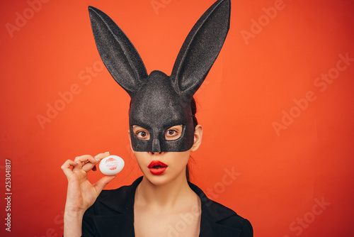 Lipstick kiss print. Red lip imprint on easter egg on red background. Print of red lips on white egg. Lips and Easter, Lipstick kiss imprint on easter egg. Bunny mask woman.