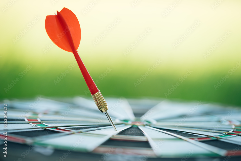 Red dart arrows hitting in the target center of dartboard with green nature background. Target business, achieve and victory concept. Red dart arrows hitting in the target center of dartboard with green nature background. Target business, achieve and victory concept.
