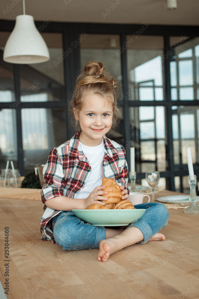 Little girl (daughter) in the morning have fun in the kitchen and eat croissant and drink tea Little girl (daughter) in the morning have fun in the kitchen and eat croissant and drink tea
