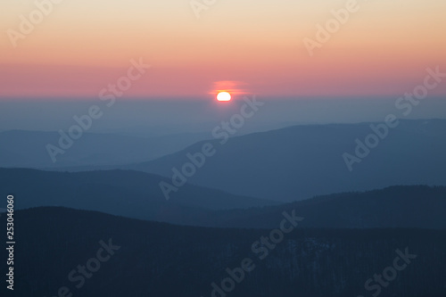 sunrise in the Carpathians on the background of blue mountain ranges and solar disk on the horizon. 