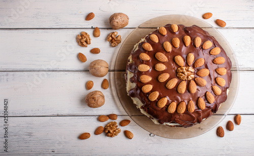 Homemade chocolate cake with almonds on white wooden background.