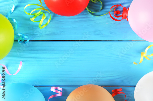 Minimal style composition with different pastel color air balloons with streamer ribbons on blue wood textured background with a lot of copy space for text. Top view, close up, flat lay.