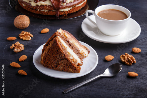 Homemade chocolate cake with milk cream, caramel and almonds on black wooden background. cup of coffee.