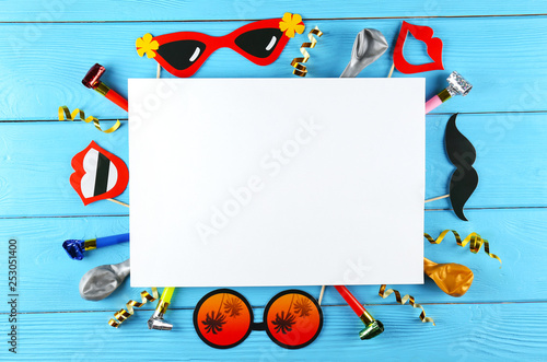 Photo booth props & blank greeting card on blue wood background. Paper moustache, lips & glasses on stick. Party kit for birthday, wedding or corporate event celebration. Flat lay copy space, top view