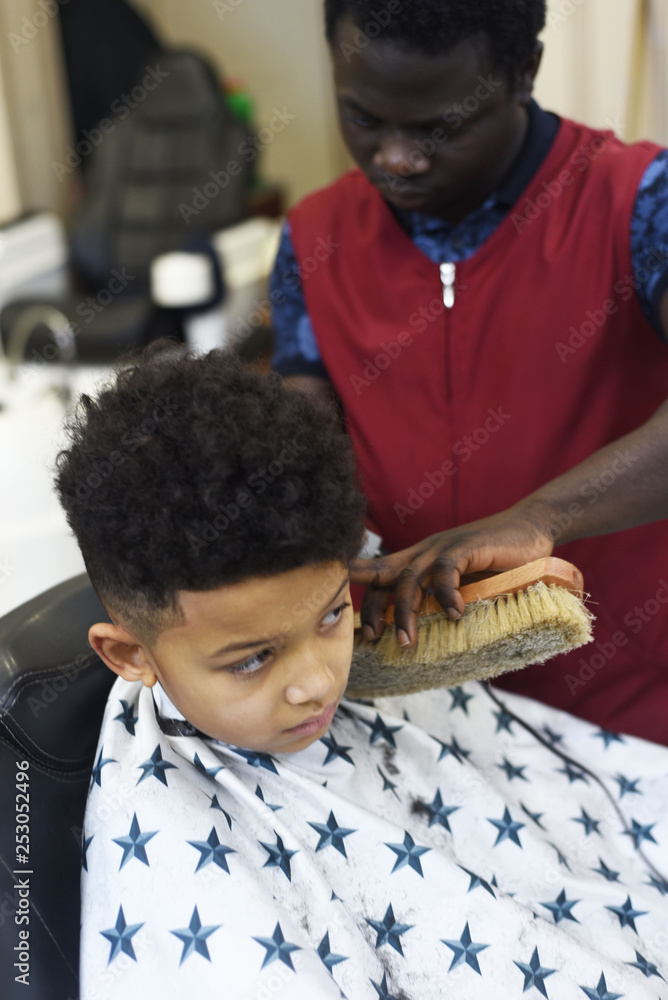 Cute african american boy in the african barbershop. Cute mixed boy makes a  haircut in the