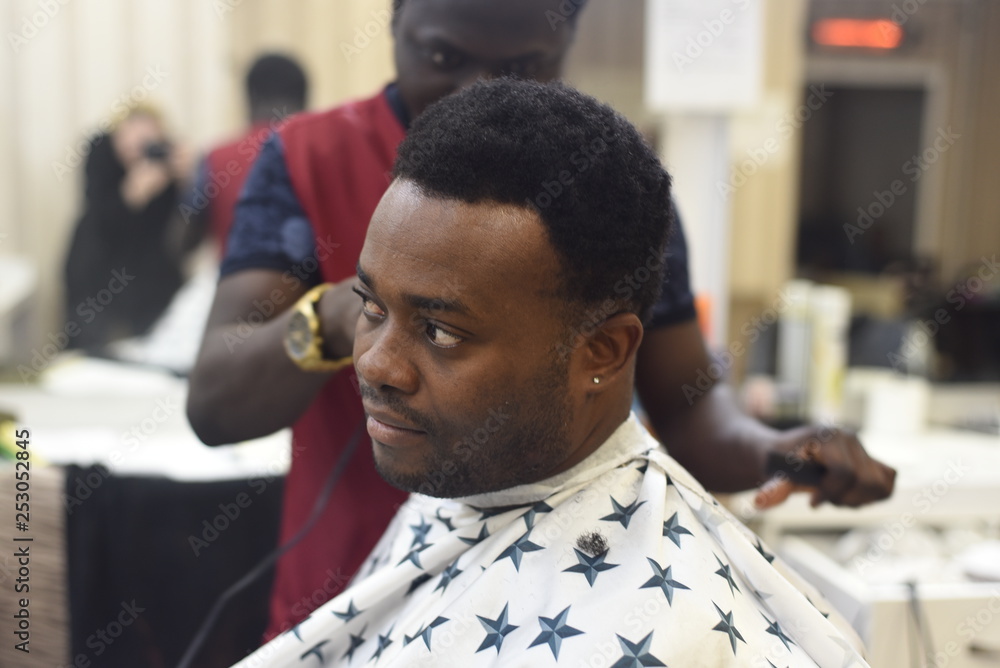 Black man in the african barbershop. Cute black man makes a haircut in the  African salon. Hair style. Haircut by machine for adults. Stock Photo |  Adobe Stock