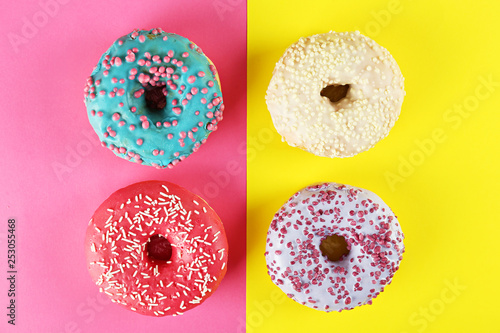 Top view composition of lush donut with colorful sprinkled icing, on bright paper textured background with a lot of copy space for text. Tasty but unhealthy food concept. Close up, flat lay, frame.