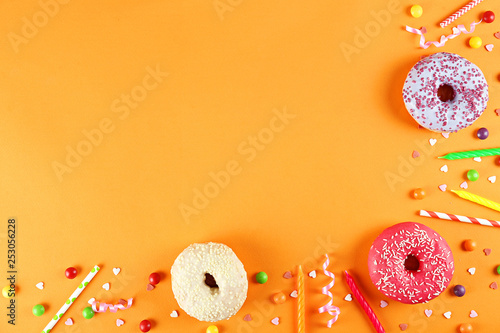 Top view composition of lush donut with colorful sprinkled icing, on bright paper textured background with a lot of copy space for text. Tasty but unhealthy food concept. Close up, flat lay, frame.