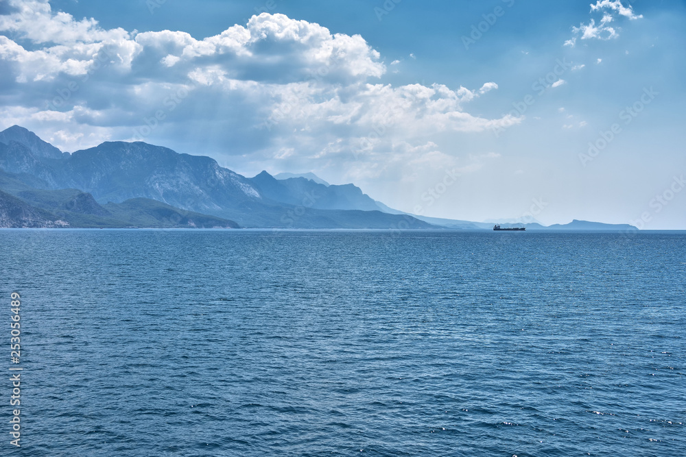 Sea coast covered with mountains in a light haze, the silhouette of the ship on the horizon