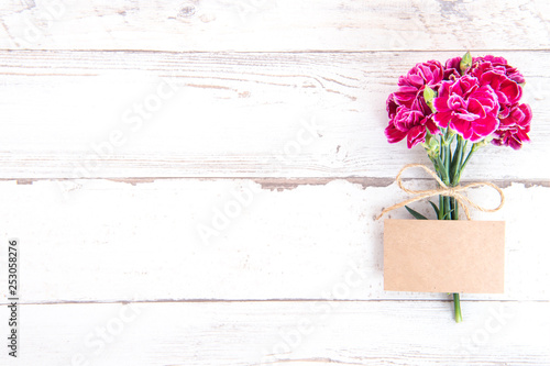 May mothers day concept photography - Beautiful carnations with template card isolated on a bright wooden table, copy space, flat lay, top view, mock up