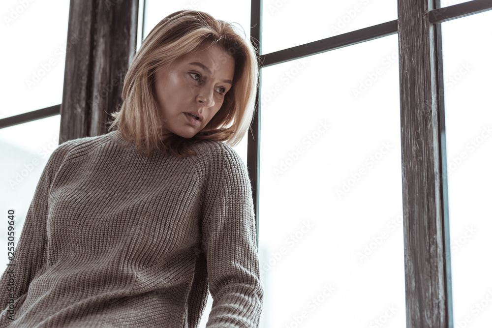 Stressed woman wearing sweater sitting near the window