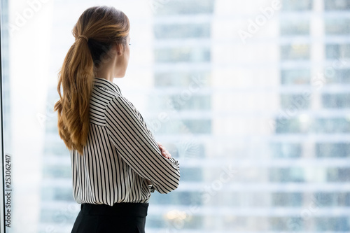 Rear view at confident rich businesswoman looking forward through window
