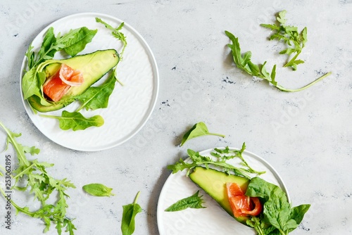 Ripe avocado boats with slices of salted trout, salmon and fresh greens on a gray background. Avocado boats stuffed with salmon with lime, spinach leaves and arugula, concept healthy food, diet.