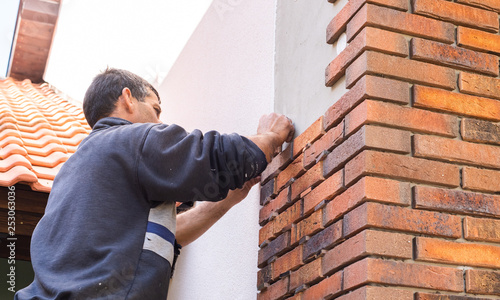 Worker putting red bricks on the house wall