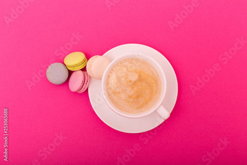 Cozy morning breakfast. Cup of coffee and colorful macaron on pink background top view. Fashion flat lay. Sweet macaroons.