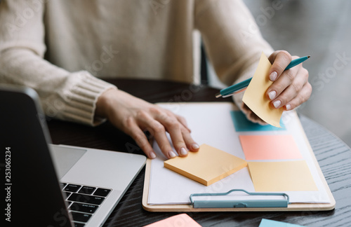 Closeup shot of university student hand holding pen, sticky note on planning board, exam preparation, learning language. Woman working start up project at workplace using scrum for productivity