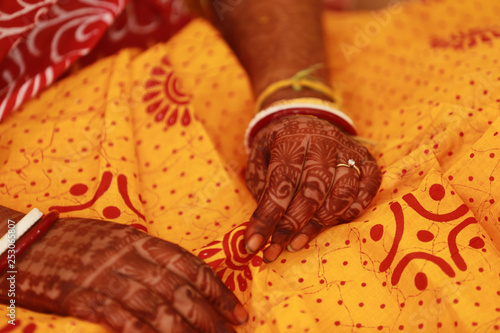 Hands of a Bengali bride showing her henna tattoo - mehendi, saakha, polla (red and white bangles) and wedding ring against her yellow red saree in the background in Kolkata, Delhi, India