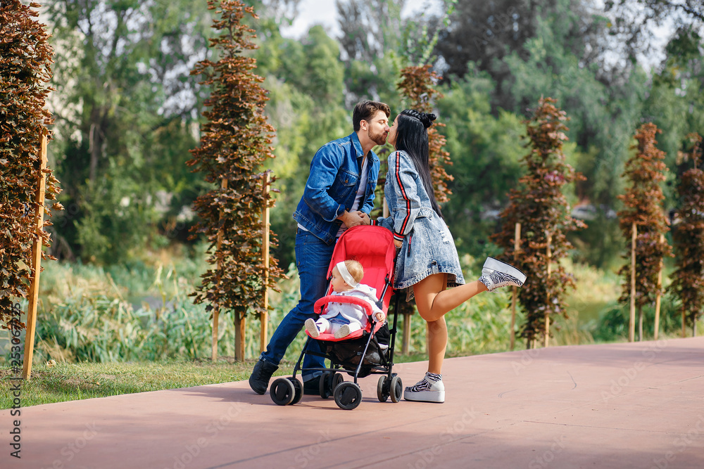 Obraz premium mom and dad are walking in the park with their daughter in a stroller, a beautiful sunny day, a beautiful family