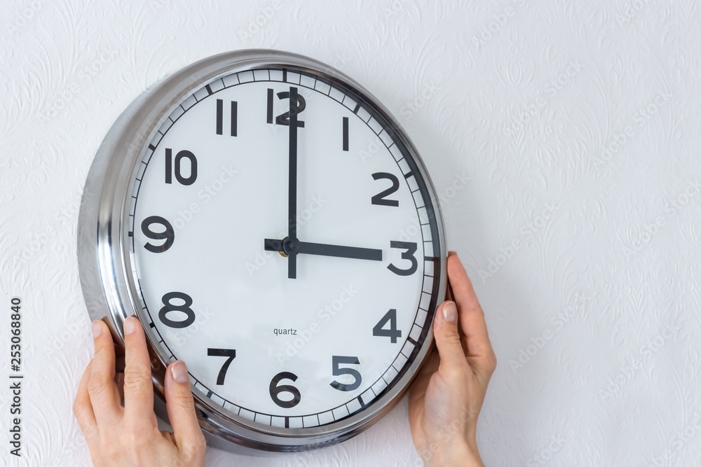 Woman hangs a big silver clock on the white wall Woman hangs a big silver clock on the white wall