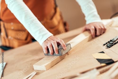 Female carpenter manually sanding wooden plank