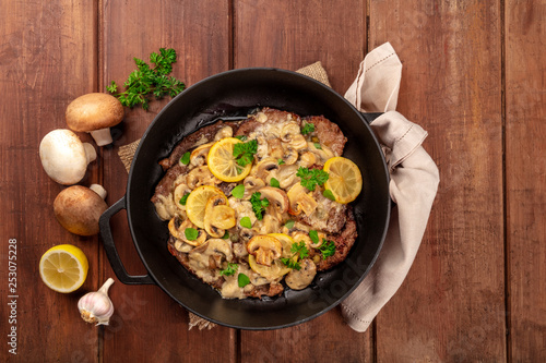 Scallopine di vitello, veal scallopini, with a mushroom sauce, lemons, and parsley, shot from the top in a pan with ingredients and copy space
