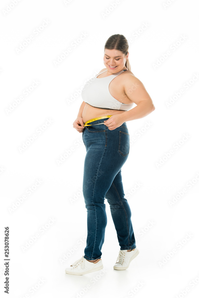 smiling overweight woman in jeans measuring waist with measuring tape isolated on white, body positivity concept smiling overweight woman in jeans measuring waist with measuring tape isolated on white, body positivity concept
