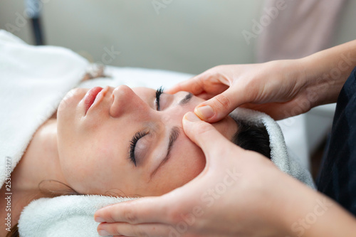 Closeup face of young woman having facial massage at spa.