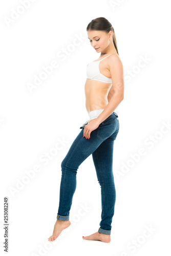 side view of slim woman in underwear taking off blue jeans isolated on white