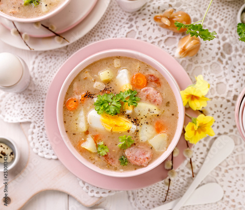 The sour soup (Żurek), polish Easter soup with the addition of sausage, hard boiled egg and vegetables in a ceramic bowl, top view. Traditional Easter dish in Poland
