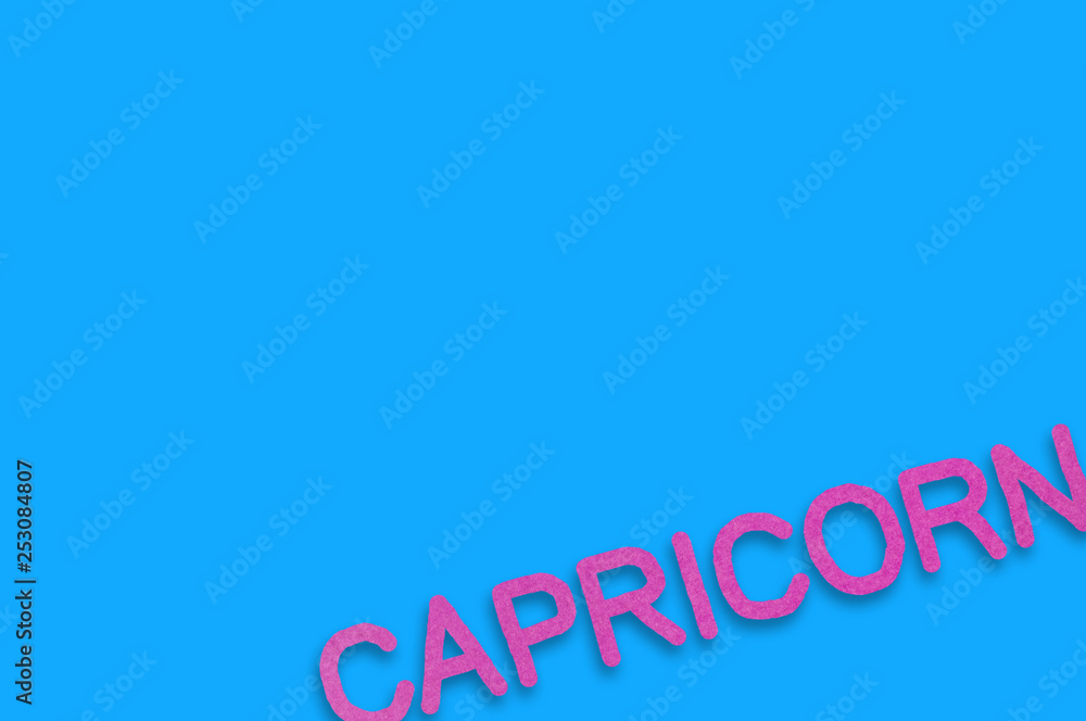 Fototapeta premium Word capricorn cut out of purple paper on blue table. Top view. Horoscope concept