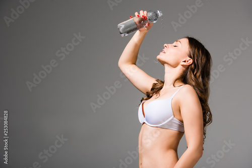 pretty young woman in underwear pouring water on face on grey background