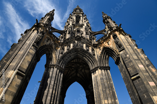 Looking up to the soot stained stones of the Sir Walter Scott Monument of Victorian Gothic architecture in Edinburgh Scotland UK with blue sky