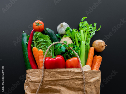 fresh organic vegetables in brown paper bag against dark table background