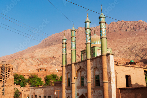 The facade of the mosque at the Uyghur village of Tuyog, with mountains on the background, Xinjiang region, China. photo