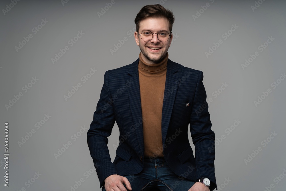 Fototapeta premium portrait of a young fashion man sitting on a chair and looking into the camera on a gray background.