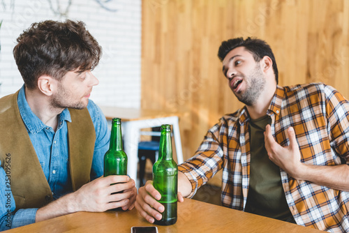 handsome men holding glass bottles of beer and talking at cafe
