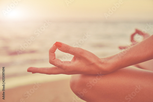 Young woman practicing yoga on the beach. Focus on hand.