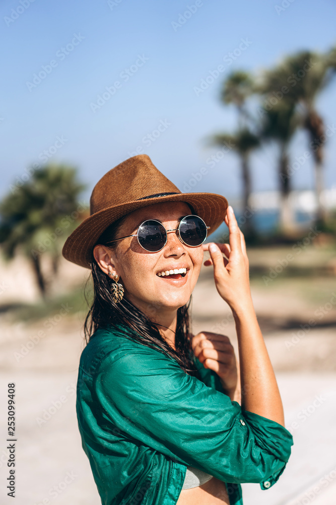 Cute pan asian girl in hat and sunglasses in green pareo walking on the seaside.