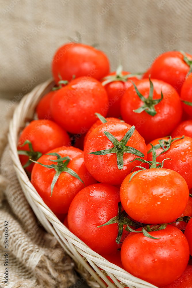Small red tomatoes in a wicker basket on an old wooden table. Ripe and juicy cherry Small red tomatoes in a wicker basket on an old wooden table. Ripe and juicy cherry