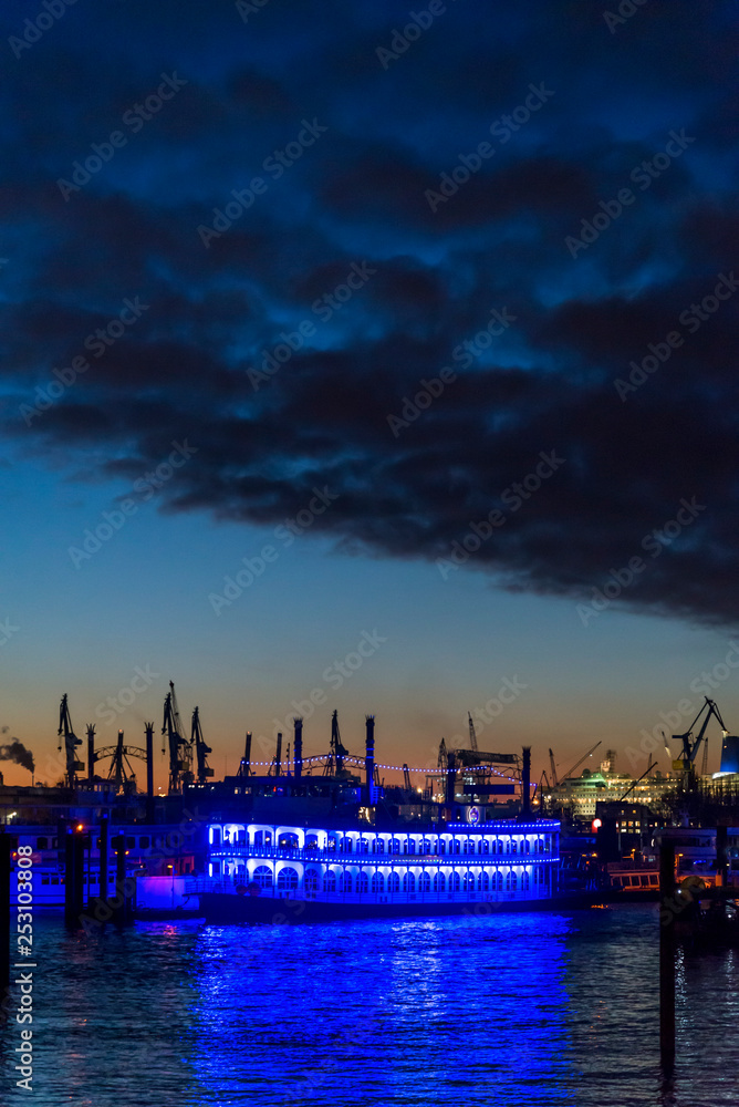 Illuminated boat and silhouetted cranes behind it at dusk in the Central Harbour on the Elbe river, Hamburg, Germany