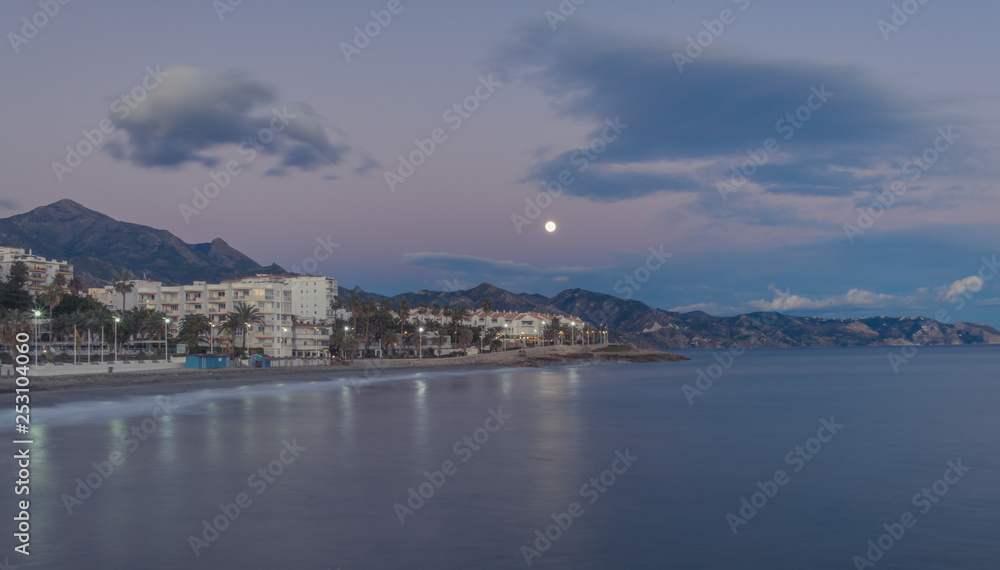 Nerja, Malaga, Andalusi, Spain - January 20, 2019: Moon at the beginning of the night over the coastal town of Nerja, southern Spain