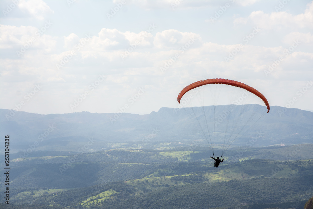 Lone paraglider gliding through the air over a green, mountainous backdrop and partially clouded skies. Lone paraglider gliding through the air over a green, mountainous backdrop and partially clouded skies.