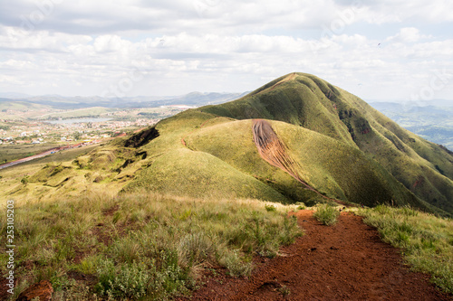 Green landscape with a road crossing it. Lake and a suburban neighborhood seen on the back. Partially clouded skies.