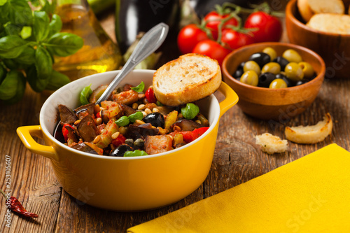 Traditional Italian caponata, served with croutons in a yellow, sunny pot. Decorated with basil and pine nuts.