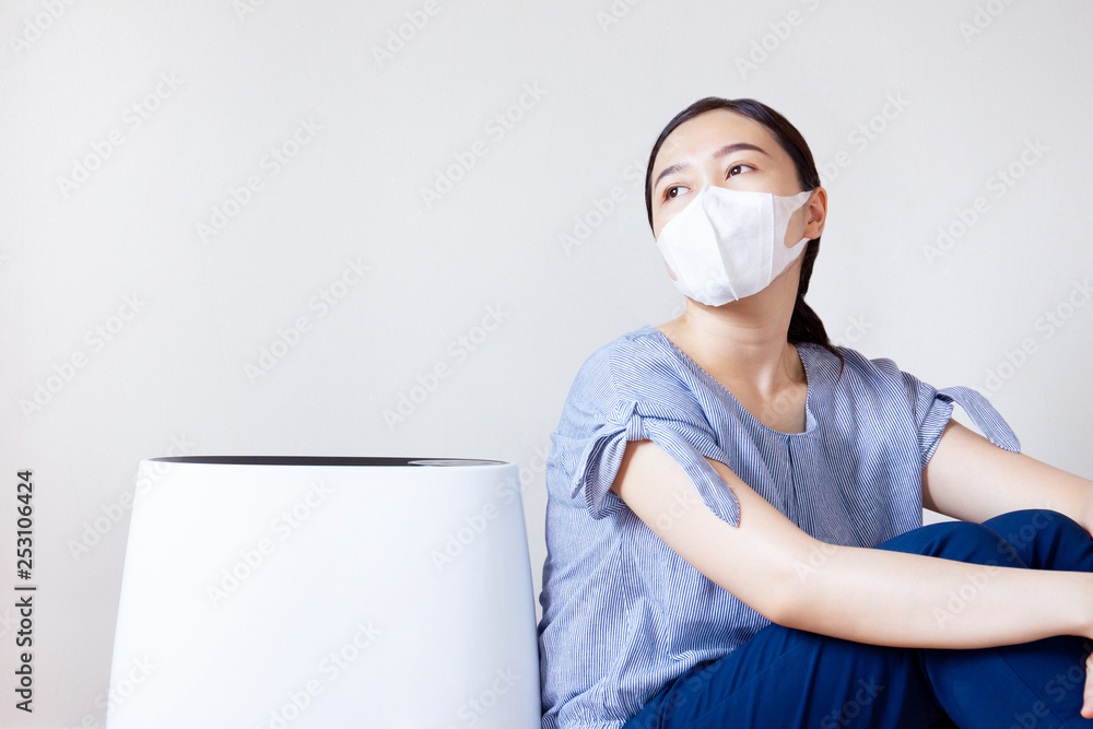 Masked Asian women sitting beside the air purifier close up. Pollution and unhealthy life concept. Masked Asian women sitting beside the air purifier close up. Pollution and unhealthy life concept.