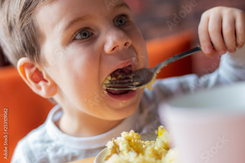 The little boy himself eats food from the fork in a cafe. Family holidays  mother and her son have a rest in the restaurant  drink cocoa and eat cake. selective focus  noise effect